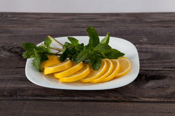 Slices of fresh juicy lemon with mint leaves on small plate on old dark grey rustic wooden table. Ingredients for homemade lemonade.
