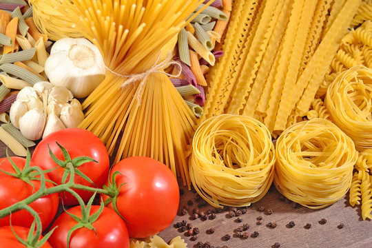 Uncooked Italian pasta, ripe tomatoes branch, garlic and black p