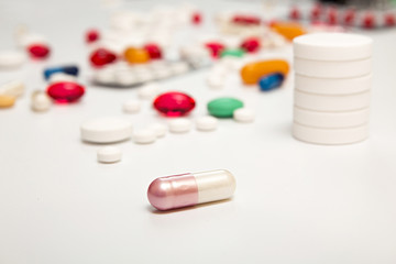 White pink medicine capsul on foreground. Heap of tablets backgr