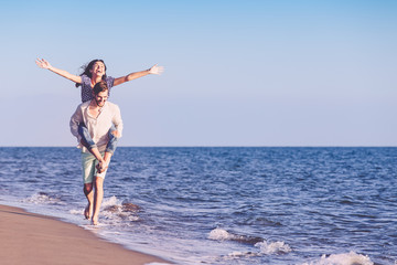 Handsome man giving piggy back to his girlfriend at the beach