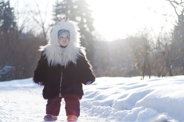 Little girl in a fur coat walks in the park on a sunny winter da - 134303223