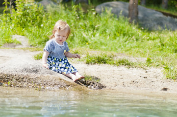 Little girl sitting on a river bank in the summer