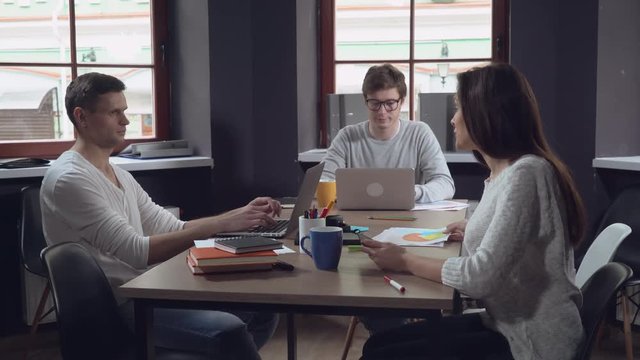 Chief of department discussing with staff new project. Young businessman wearing in eyeglasses sitting at the working place typing on computer. Caucasian smiling employees talking