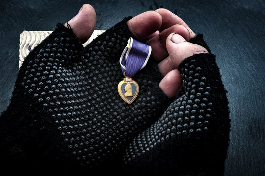 Homeless veterans and social issues concept with grunge image of dirty hands of a homeless man wearing fingerless gloves and holding a purple heart medal