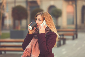 Fototapeta premium Attractive woman using cellphone and drinking coffee outdoors.
