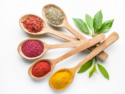 Assortment of colorful spices in the wooden spoons on the white