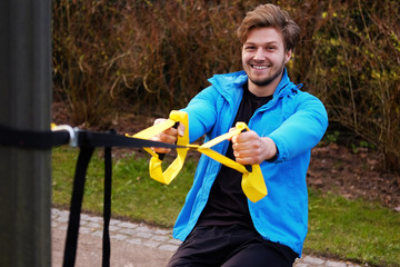 Attractive positive male exercising with trx fitness strips.