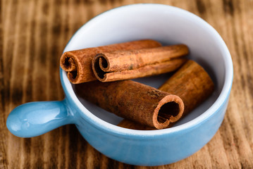 Whole cinnamon inside blue enameled cast iron pot standing om wooden board.