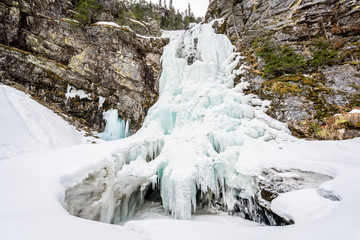 Fototapeta na wymiar Frozen waterfall on bare mountain with deep snow on the ground.