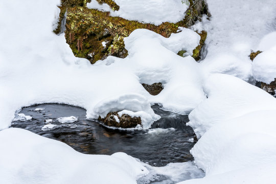 Winter stream with deep snow and water flows underneath. Early spring with melting snow.