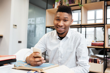 Fototapeta premium Handsome african student in library chatting by his phone.