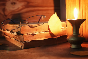 old tattered book on a wooden table lighted candle and glasses