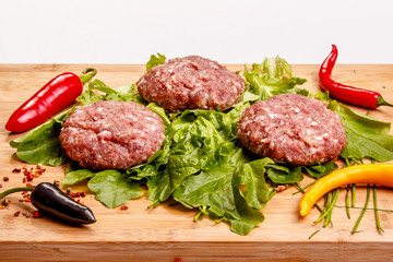 Raw beef burgers with peppers and greens are on the Board.