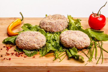 Raw beef burgers with peppers and greens are on the Board.