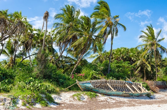 Abandoned shipwreck stranded on a sandy beach under palm trees and deep blue sky on a 