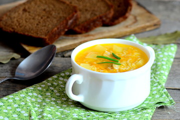 Easy rice soup. Home rice soup with meat, potatoes and carrots in a bowl. Bread pieces, spoon, green napkin on old wooden table. Dinner or lunch dish. Closeup