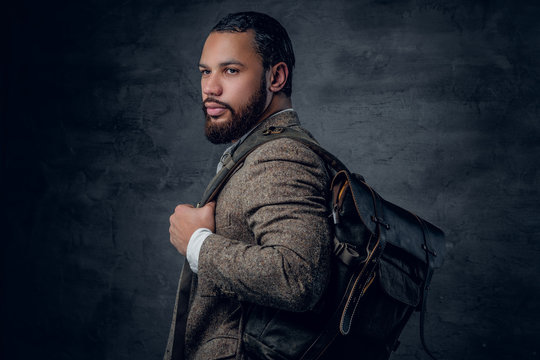 Black man in a suit holds backpack.