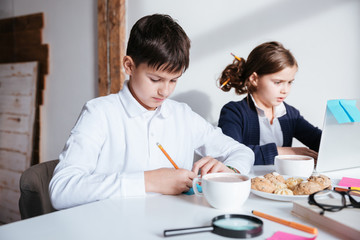 Serious little children using laptop and having breakfast