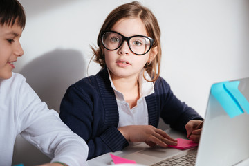 Beautiful little girl in glasses writing and using laptop