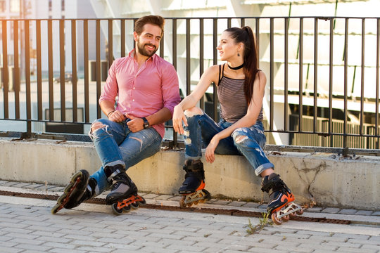 Couple on rollerblades sitting. Guy smiling to a girl. Original idea for first date.