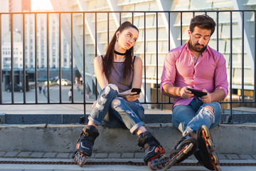 Couple with phones is sitting. Bored woman looking at man. Who are you texting.