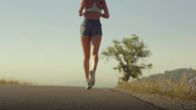 Fit young woman in sport shorts and running shoes going for refreshing morning jog on the road. Healthy lifestyle, health care, body care, calories burning, willingness concept. Low angle rear view.