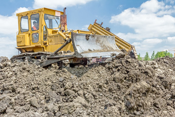 Heavy earthmover is moving earth at building site. Dump truck is