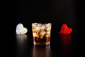 Hearts and glass of alcohol on black table