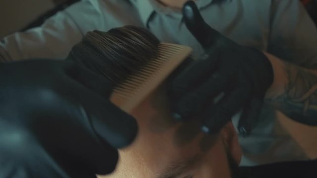 Attractive dark haired man wearing white shirt doing a haircut with hair dryer and hair brush for man looking at the camera.