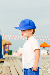 Baby boy in blue cap with sad and resent emotion. Frown baby boy on the stone beach in summer...