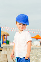 Baby boy in blue cap with sad and resent emotion. Frown baby boy on the stone beach in summer vacation