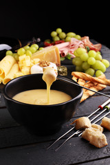 Gourmet Swiss fondue dinner on a winter evening with assorted cheeses on a board alongside a heated pot of cheese fondue with two forks dipping bread and white wine behind in a tavern or restaurant