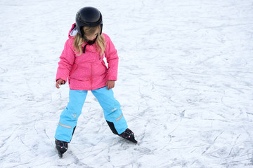 Fototapeta na wymiar Happy little girl skating in winter outdoors, wearing safety helmet 
