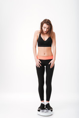 Fototapeta premium Shocked young fitness lady standing on scales