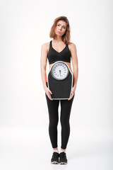 Sad funny young fitness lady holding scales