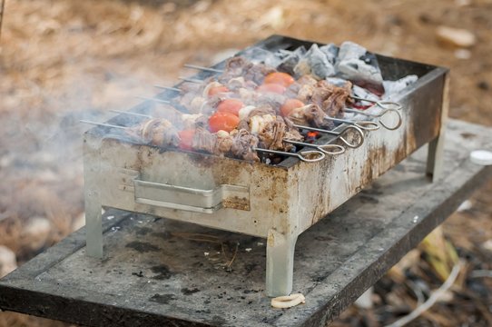 Grilled shish kebab on metal skewer closeup. Smoking beef meat and cherry tomatoes on a skewer in a steel brazier.