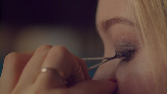 Applying false eye lashes macro close up 4k shallow dof. Hand of professional makeup artist sticking individual eyelashes to done and prepared eyelid of model with tweezers. Glamour fashion secrets