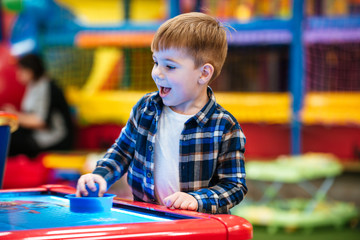 Fototapeta na wymiar Cheerful little boy playing air hockey game at indoor playground