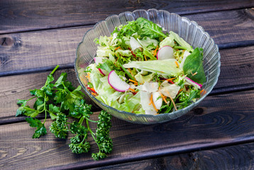 Spring and summer fresh salad with vegetables, radish, carrot, parsley, salad lettuce, beet, beetroot, rocket on old dark grey rustic wooden table. Healthy vegetarian food.
