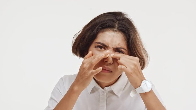 Young beautiful brunette east asian female in shirt discontentedly looking at camera trying to make face better on white background