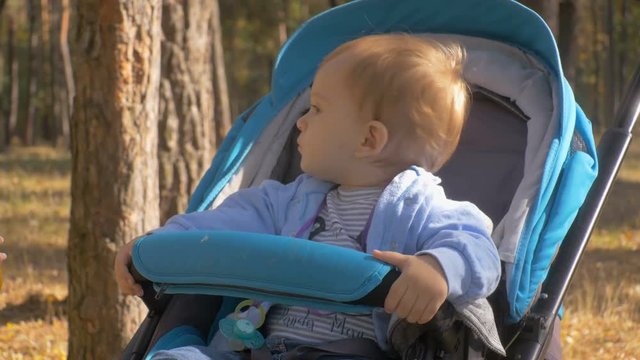 Closeup footage of young mother feeding her baby boy sitting at stroller