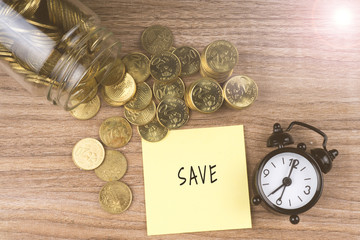 Coins spilling out of a glass jar with save text on wooden background. Financial Concept