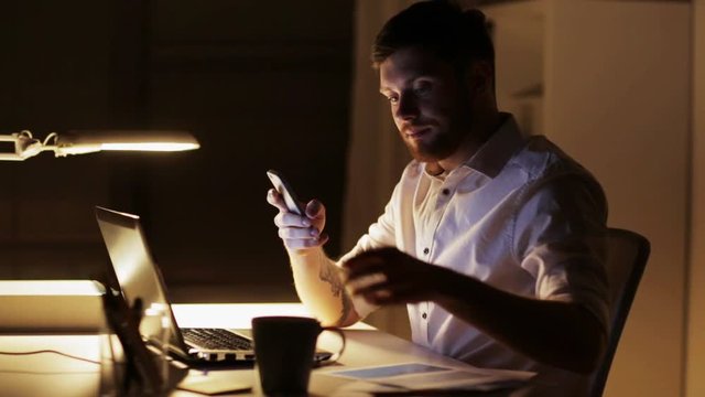 man with laptop and smartphone working at night office
