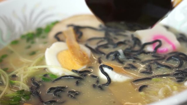 Hand eating hot Japanese ramen, black noodle with boiled egg in flavorful soup