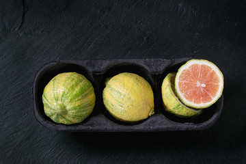 whole and sliced citrus fruit pink tiger lemon in paper market box over black stone slate textured...