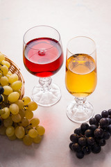 Wine and grapes. White and red wine in glasses on light marble b