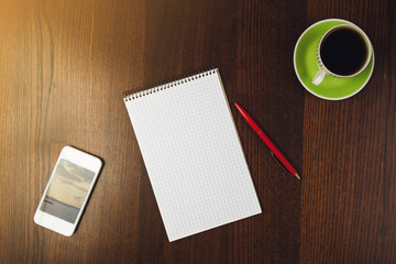close-up pencil on blank notepad near phone and cup of coffee at wooden desk