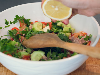 Hand squeezing lemon juice into a bowl of tuna salad.