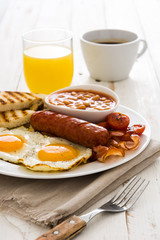 Traditional full English breakfast with fried eggs, sausages, beans, mushrooms, grilled tomatoes and bacon on white wooden background
