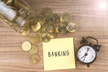 Coins spilling out of a glass jar with BANKING text on wooden background. Financial Concept